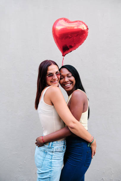 istock Cheerful lesbian couple hugging while holding a red heart-shaped balloon. 1338208257
