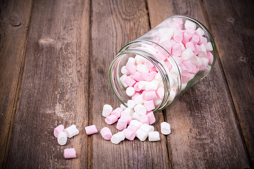 Pink and white marshmallows spilling from a storage jar, over old wood background. Vintage effect with intentional vignette