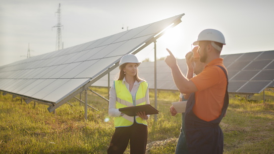 Three solar energy specialists at a solar power facility. Professional engineers discuss innovative project. Team of industrial technicians in solar park. Construction of solar power plant