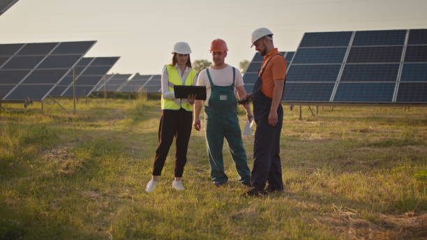 istock Three solar energy specialists at a solar power facility. Two small children run to their parents who are at work. A solar power plant employee with children at work smiling at the camera. Happy 1338214956