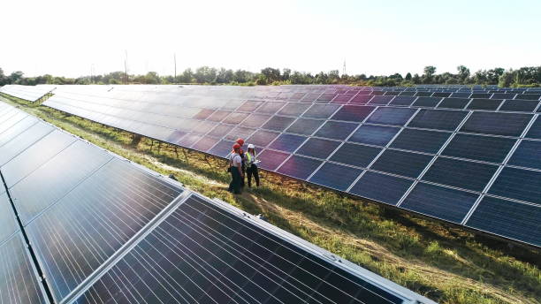 trois spécialistes de l’énergie solaire marchant dans une centrale solaire. des ingénieurs professionnels discutent d’un projet innovant. images aériennes de centaines de modules ou de panneaux d’énergie solaire. équipe de collègues - solar panel engineer solar power station women photos et images de collection