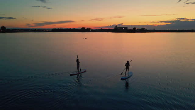 Rear view of two women kayaking on river during sunset