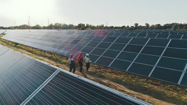 vista superior de especialistas caminando a través de una planta de energía solar. tres empleados de una planta de energía alternativa caminando y hablando sobre el esquema de paneles solares - solar panel engineer solar power station solar energy fotografías e imágenes de stock