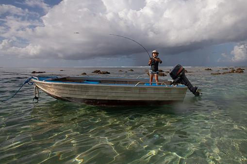 A small boy fishing shallow water in a dingy