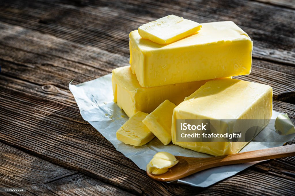 Butter blocks and pieces on wooden table. Copy space High angle view of various sticks of fresh butter with slices shot on rustic wooden table. The composition is at the right of an horizontal frame leaving useful copy space for text and/or logo at the left. High resolution 42Mp studio digital capture taken with Sony A7rII and Sony FE 90mm f2.8 macro G OSS lens Butter Stock Photo