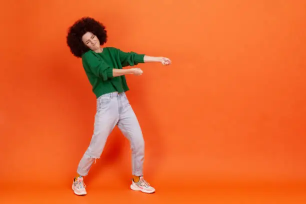 Photo of Full length profile portrait of woman with Afro hairstyle in green sweater pulling invisible heavy burden, striving hard to achieve success.