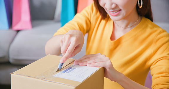 close up of happy asian woman receive packing parcel after online shopping and opening a delivery box in the living room at home