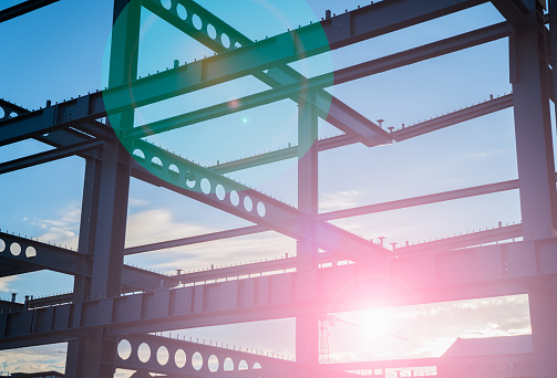 Sunrise lens flare through construction steel framework in silhouette against blue sky.