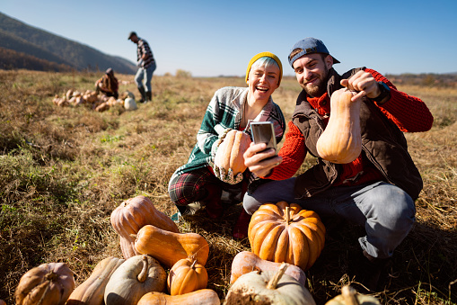 Cheerful young Caucasian couple, farm workers, making selfie with the smart phone on the field after harvesting.