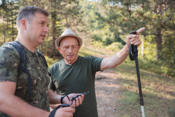 hiker holding a compass and elderly man showing the direction - explorer tourist frowning men imagens e fotografias de stock