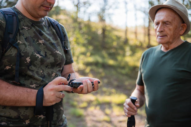 tired senior hiker observing son using compass - explorer tourist frowning men imagens e fotografias de stock