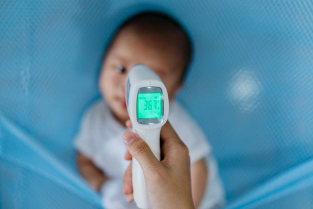 madre che controlla la temperatura corporea del suo bambino - infrared thermometer foto e immagini stock