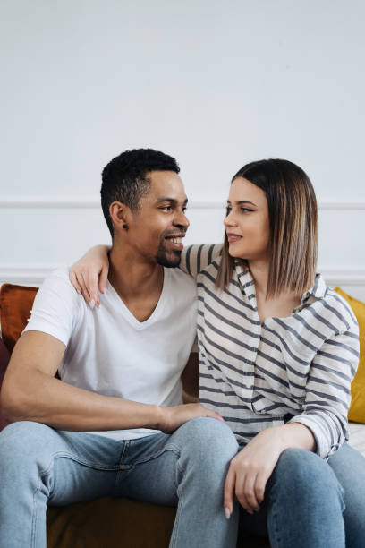 istock Front view of young diverse couple sitting on a couch at home 1338264249