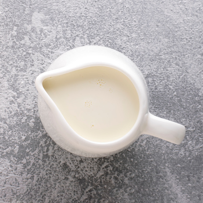 Milk jug with milk on a gray concrete background, top view, close-up.