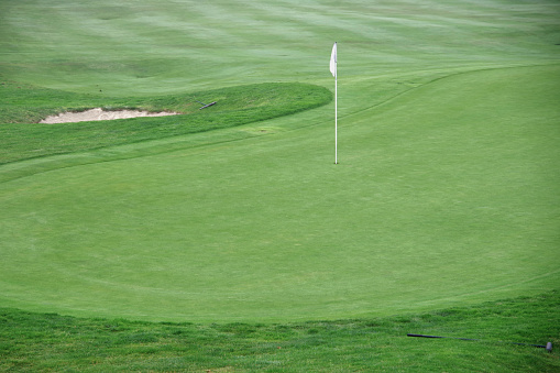 White flag on a golf course marking the hole on a green with a sand trap near by