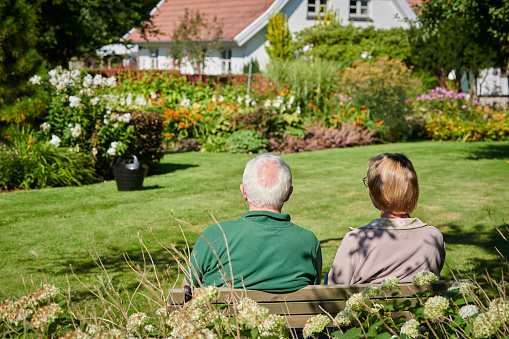 Couple sitting on a bench in their big well kept garden enjoying the view
