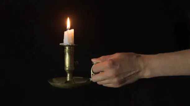 Photo of Decorative copper candlestick with burning candles in a female left hand on a black background