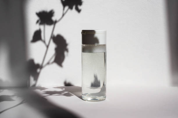 istock Bottle with clear micellar water on a white background with a shadow from flowers. Lotion for cleansing the skin and eyes from cosmetics, makeup. Beauty product in white plastic packaging. 1338289657