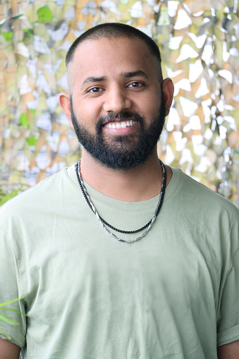 Stock photo showing headshot of Indian man with shaved head wearing t-shirt and necklaces.