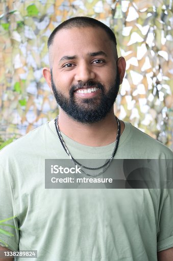 istock Close-up image of Indian man with buzz cut hairstyle to disguise receding hairline, wearing t-shirt with necklace, posing looking at camera 1338289824