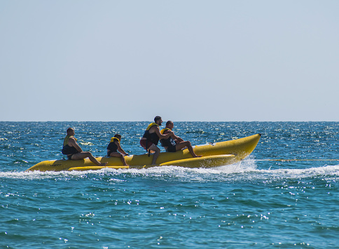 Group of men who feel good on an inflatable banana pulled by a skyjet on the sea waves. Romania, Jupiter. August, 21, 2021