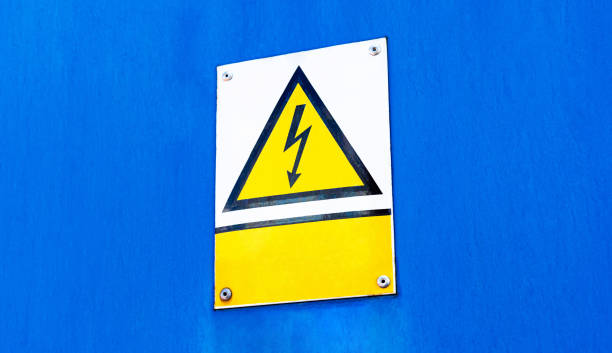 istock Metal plate sign with a worn yellow high voltage warning triangle symbol and an empty blank text box, blue background, copy space. Electricity, electrocution danger, hazard abstract concept, closeup 1338295960