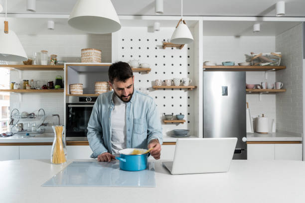 istock Young smiling man cooking spaghetti pasta for dinner in the home kitchen while listening music on his laptop and having a good time alone 1338297631