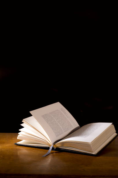 istock Open book or Bible on highly polished wood table.  Black background. 1338298028