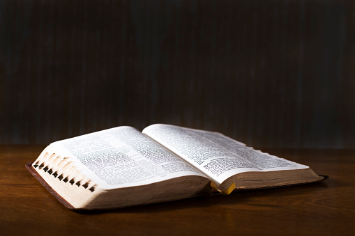 Open book or Bible on highly polished wood table.  Black background.  Reflection in table and there is a satin bookmark inside the book.