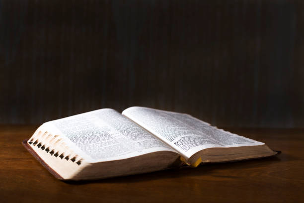 Open book or Bible on highly polished wood table.  Black background. stock photo