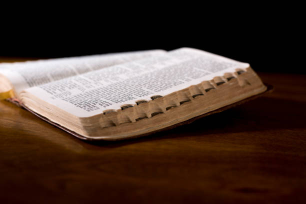 istock Open book or Bible on highly polished wood table.  Black background. 1338298087