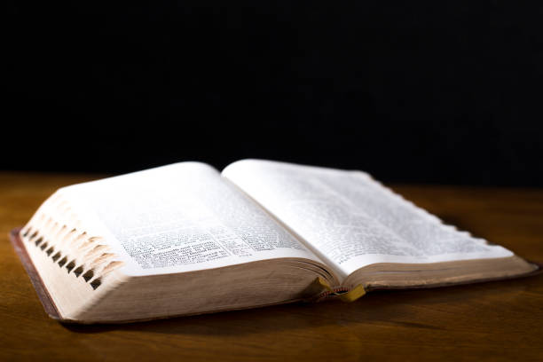 istock Open book or Bible on highly polished wood table.  Black background. 1338298098