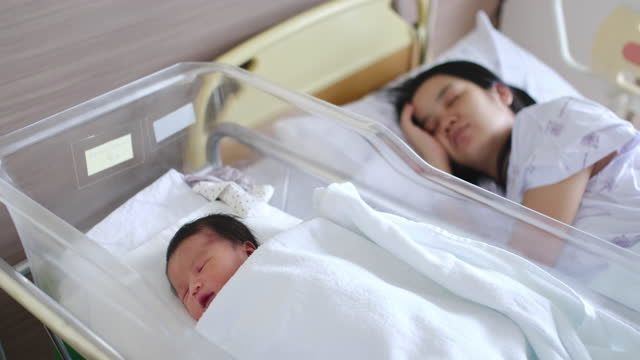 Asian mother sleeping with newborn baby at hospital