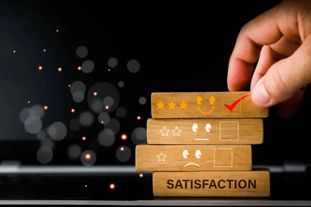 Photo of The concept is the best excellent business services rating customer experience and satisfaction survey. The hand of a businessman chooses a smiley face and 5 Star icon on a woodblock.