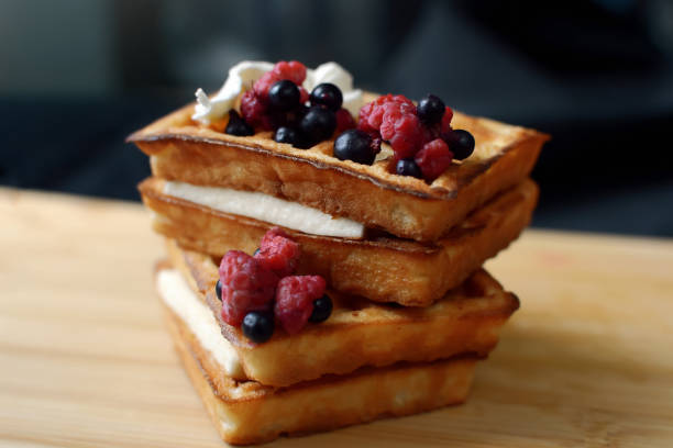 Delicious appetizing waffles with creamy white cream, garnished with raspberries and black currants, just cooked, waiting to be tasted for dessert, close-up photo.