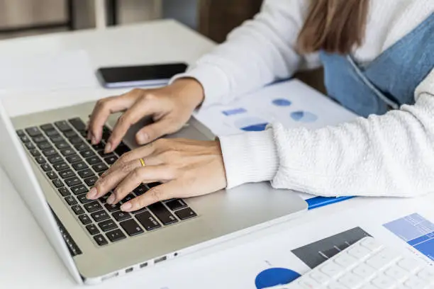 Photo of A businesswoman typing on a laptop, she is talking to an employee using a laptop messenger to inquire about company finances. The concept of using technology to assist in communication.