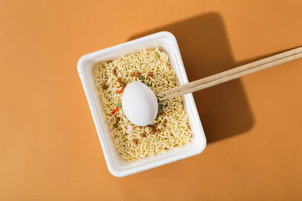 Instant noodles with fresh egg in a white plastic plate, on an orange background