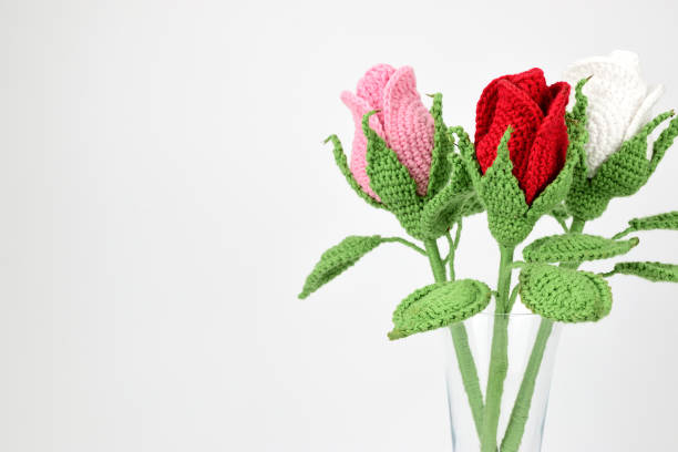 Three knitted roses in a glass beaker isolated on a white background.