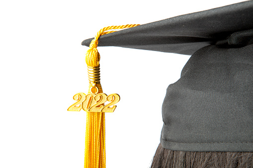 A close up of a class of 2022 tassel hanging from a black graduation cap isolated on a white background.