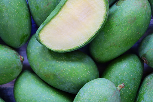 Stock photo showing close-up, elevated view of pile of fresh, whole, tropical raw mango fruit with one sliced in half.
