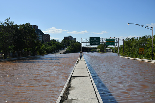 New Brunswick, NJ USA - September 2, 2021: City of New Brunswick flooded after Hurricane Ida. Woman walks on median in the middle of a flooded route 18 highway in New Brunswick, NJ after Hurricane Ida.