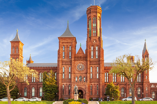 Founded in 1846, the Smithsonian is the world's largest museum and research complex, consisting of 19 museums and galleries. Currently the Smithsonian Castle houses the administrative offices and the main Smithsonian visitor center. Sightseeing tourists and blue sky with clouds are in the image.