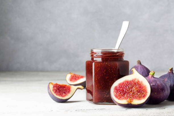 istock Fig jam in a glass jar on a light gray table. Fruit canning and storage. Jam for cheese and bruschetta. Space for text 1338323571