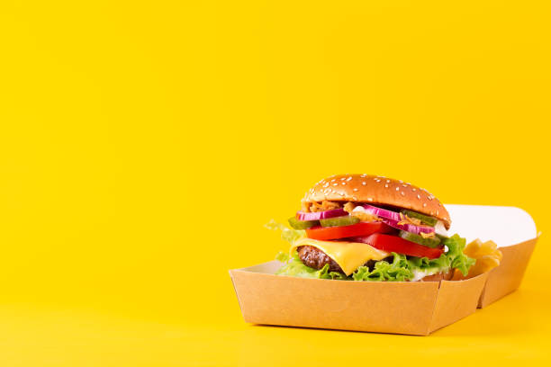 istock Burger with a marble beef patty in open paper package on a yellow background. Space for text. 1338323714
