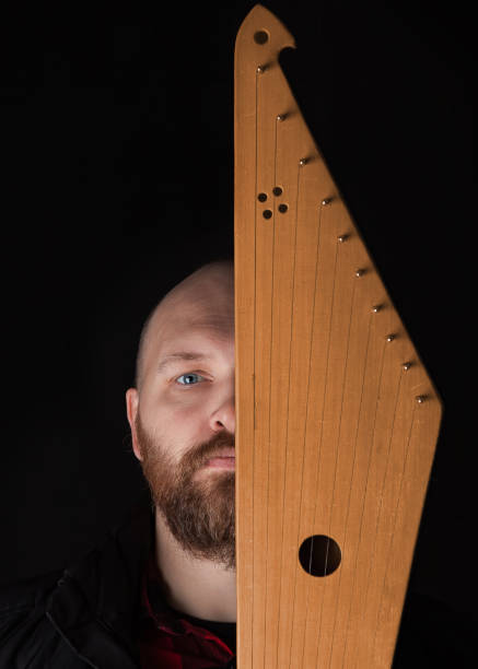 Bearded man hides his face behind Kantele, a national Finnish and Karelian musical instrument, also known as the psaltery (gusli) in Russia and as the kankles, kokle, and Kannel in the Baltic States. Bearded man hides his face behind Kantele, a national Finnish and Karelian musical instrument, also known as the psaltery (gusli) in Russia and as the kankles, kokle, and Kannel in the Baltic States. psaltery stock pictures, royalty-free photos & images