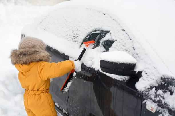 un bambino piccolo pulisce la neve dal finestrino di un'auto dopo una forte nevicata - snow car window ice scraper foto e immagini stock