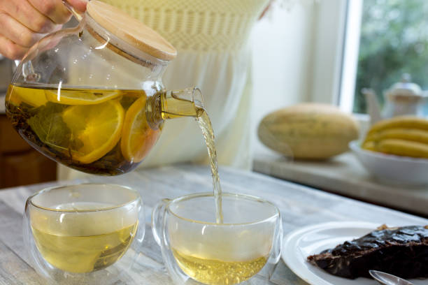 istock Woman pours fresh brewed tea with mint and lemon into a cup. Tea drinking process. 1338334431