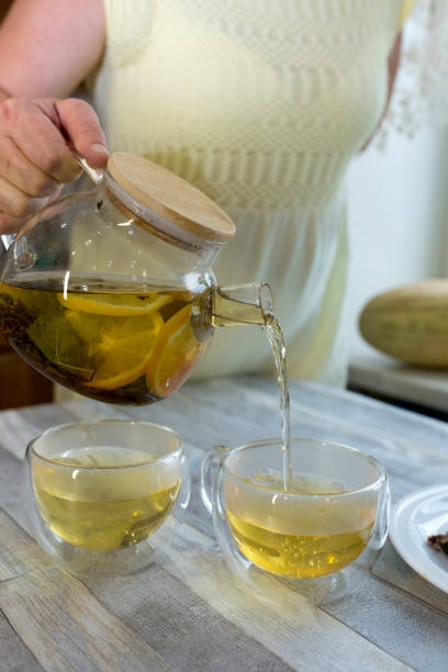 istock Woman pours fresh brewed tea with mint and lemon into a cup. Tea drinking process. 1338334433