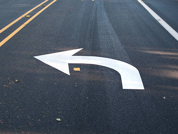 White turn left arrow painted on asphalt Arrow indicating upcoming turn. Newly painted on fresh asphalt. Good concept shot for change, modern life, detour, new direction, etc. left handed stock pictures, royalty-free photos & images