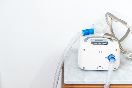 cpap machine with air hose and head mask on bedside table at home